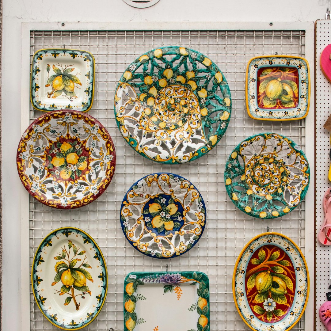 A wall of hand-painted majolica plates and platters with lemon and floral motifs, on display at a ceramic workshop in Vietri sul Mare