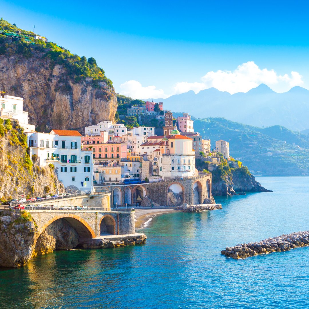 The fishing village of Atrani seen from the sea, with its bell tower and pastel houses stacked between cliff and beach, Amalfi Coast